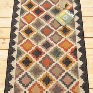 May include: A rectangular jute rug with a geometric pattern in shades of brown, orange, yellow, and black. The rug has a black border and fringe on the edges. The text "DurrieIndiaArt" is printed on the rug.