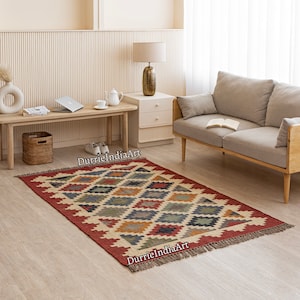 May include: A red, beige, blue, and green patterned rug with fringe on the edges. The rug is laid out on a wooden floor in a living room setting with a couch and a side table.