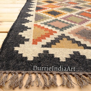 May include: Black and white geometric patterned rug with colorful accents in orange, yellow, and brown. The rug has a fringe border and the text "DurrieIndiaArt" is visible in the bottom right corner.