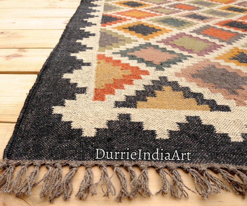 May include: Black and white geometric patterned rug with colorful accents in orange, yellow, and brown. The rug has a fringe border and the text "DurrieIndiaArt" is visible in the bottom right corner.