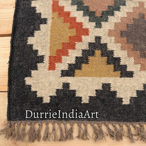 May include: Black and white geometric patterned rug with brown, orange, and yellow accents. The rug has a fringe border and the text "DurrieIndiaArt" is visible in the bottom center of the rug.