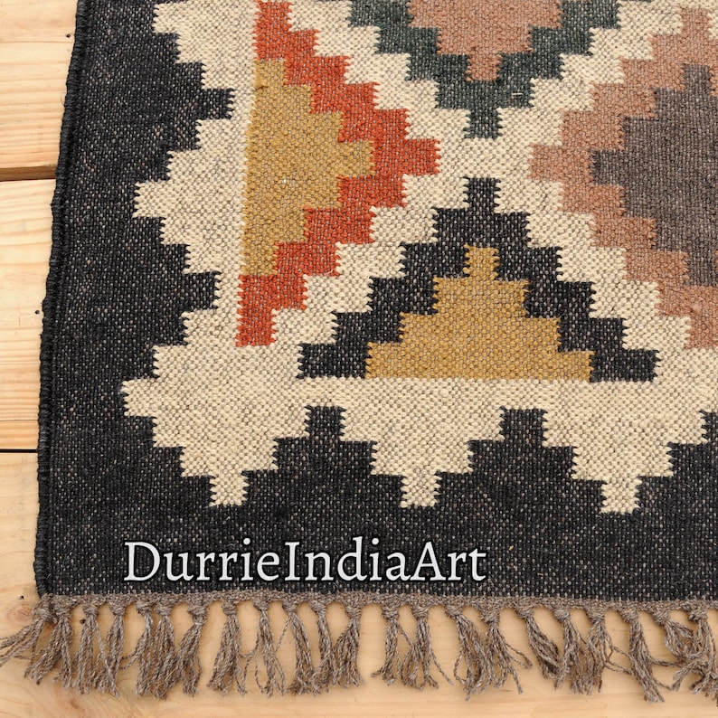 May include: Black and white geometric patterned rug with brown, orange, and yellow accents. The rug has a fringe border and the text "DurrieIndiaArt" is visible in the bottom center of the rug.
