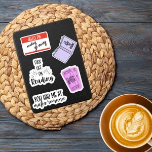 May include: A black notebook with four stickers on it. The stickers are pink and white and have text on them. The text on the stickers reads "HELLO. I'M reading go away", "FUCK OFF. I'M Reading", "YOU HAD ME AT mafia romance", and "827830 30".