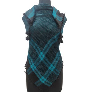 May include: A square scarf featuring a black and teal geometric pattern with diagonal stripes. The scarf has a repeating small diamond motif throughout the fabric and is finished with black tassels along the edges, draped over a mannequin.