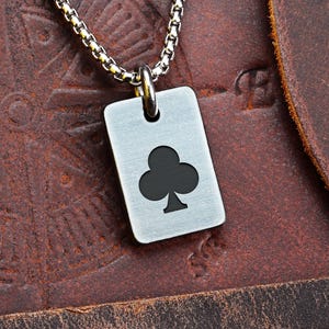 May include: A silver-tone pendant necklace featuring a rectangular tag with a black club symbol. The pendant hangs from a chain necklace. The word "FRONT" is visible in the top left corner.