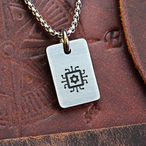 May include: A silver dog tag pendant featuring a black circuit board design suspended from a silver chain. The tag is rectangular with rounded corners. The background is a brown leather surface with a compass rose design.