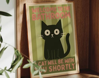 May include: A framed print featuring a black cat illustration with the text "WELCOME TO THE BATHROOM" and "CAT WILL BE WITH YOU SHORTLY" in pink and green. The print is displayed on a wooden shelf.