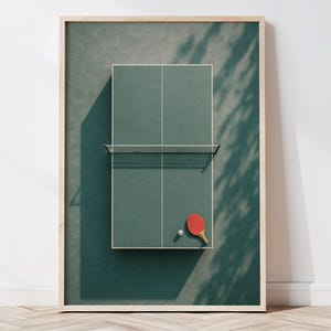 Könnte beinhalten: Gerahmter Druck mit einer grünen Tischtennisplatte mit Netz, rotem Schläger und weißem Ball. Der Druck steht vor einer weißen Wand mit Holzboden.
