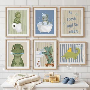May include: Six framed dinosaur-themed art prints in a bathroom setting. The prints feature cartoon dinosaurs in various bath-time activities, including bathing, brushing teeth, and using the toilet. The text "So Fresh and So Clean" is also displayed. A folded towel, soap, and baby shoes are on the counter.