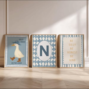 May include: Three framed art prints with a light blue and beige color scheme. One print features a goose wearing a cowboy hat and boots with the text "Silly Goose On The Loose." Another has a blue "N" on a diamond pattern. The third says "Be Silly, Be Honest, Be Kind."