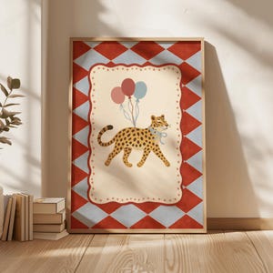May include: A framed art print featuring a leopard with balloons. The leopard has a blue bow and is walking across a cream-colored background. The background is framed by a red and blue diamond pattern.