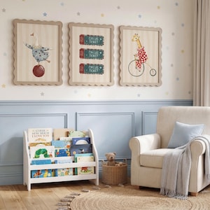 Puede incluir: Una habitaci&oacute;n infantil con obras de arte enmarcadas con tem&aacute;tica de circo, incluyendo un ganso sobre una bola, entradas de circo y una jirafa en bicicleta. Una estanter&iacute;a blanca contiene libros coloridos, y un sill&oacute;n beige con coj&iacute;n y manta azules est&aacute; cerca.