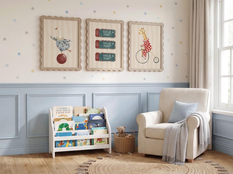 Puede incluir: Una habitaci&oacute;n infantil con obras de arte enmarcadas con tem&aacute;tica de circo, incluyendo un ganso sobre una bola, entradas de circo y una jirafa en bicicleta. Una estanter&iacute;a blanca contiene libros coloridos, y un sill&oacute;n beige con coj&iacute;n y manta azules est&aacute; cerca.