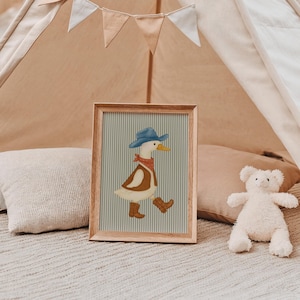 May include: A framed illustration of a cartoon duck wearing a blue cowboy hat, red bandana, brown vest, and boots. The background features a light blue and white striped pattern. The frame is made of wood.