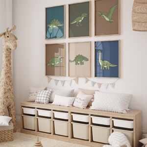 May include: A collection of six framed dinosaur art prints in a child's room. Each print features a different dinosaur illustration in green on a colored background. The room also includes a wooden storage bench with white bins, pillows, and a giraffe-shaped toy.