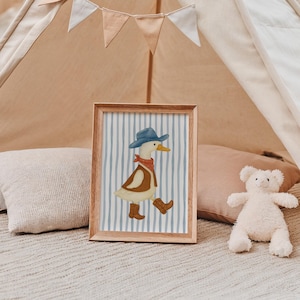 May include: A framed print featuring a cartoon duck dressed as a cowboy, wearing a blue hat, red bandana, brown vest, and boots. The background has blue and white vertical stripes. The frame is made of wood.