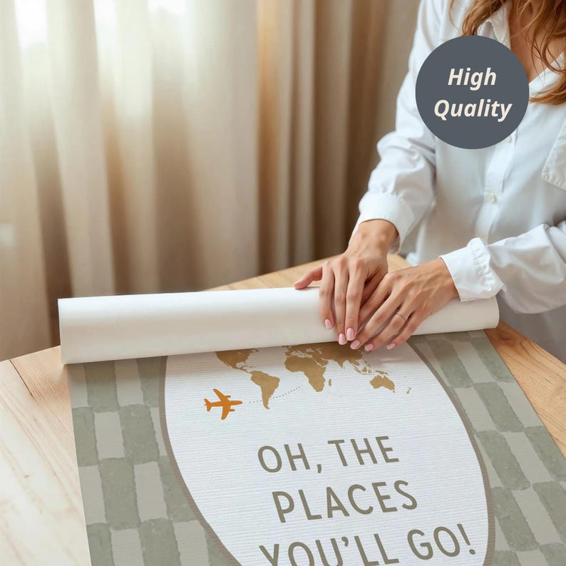 Może przedstawiać: Zwinięta mapa podr&oacute;ży z projektem mapy świata w kolorze złotym i napisem "OH, THE PLACES YOU'LL GO!". Zawiera r&oacute;wnież pomarańczową grafikę samolotu. Mapa leży na drewnianym stole.