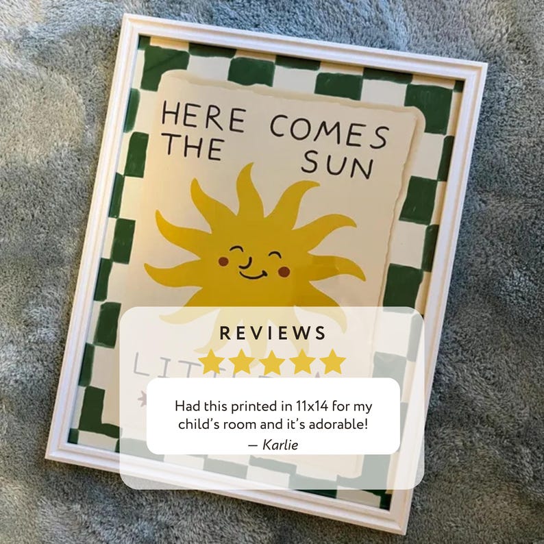 May include: A framed art print with the text "HERE COMES THE SUN" and a smiling yellow sun illustration. The frame is white with a green and white checkered border. The print is 11x14 inches.