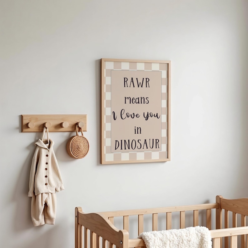 May include: A framed print with the text "RAWR means I love you in DINOSAUR" hangs on a wall. A wooden coat rack holds a beige outfit and a woven bag. A wooden crib is in the foreground.