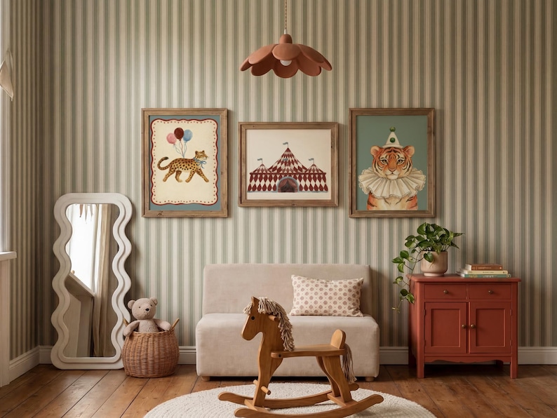 Puede incluir: Una habitaci&oacute;n infantil con tres impresiones art&iacute;sticas enmarcadas con tem&aacute;tica de circo. Las impresiones presentan un leopardo con globos, una carpa de circo y un tigre con un collar de payaso. Un caballito balanc&iacute;n de madera, un sof&aacute; peque&ntilde;o y un armario rojo completan la decoraci&oacute;n.