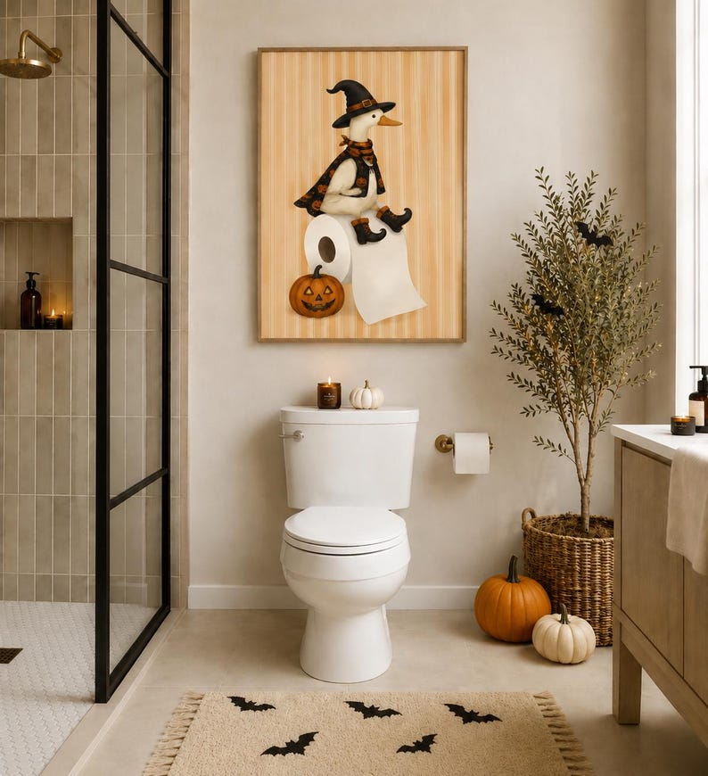 May include: A framed wall art print featuring a white duck wearing a black witch hat, cape, and boots, sitting on a roll of toilet paper next to a jack-o'-lantern pumpkin. The background of the print has vertical tan stripes.