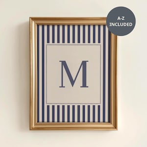 May include: Framed wall art featuring the letter "M" in navy blue on a cream background. The artwork is surrounded by navy blue and white vertical stripes and a gold frame. A circular graphic indicates that all letters A-Z are included.