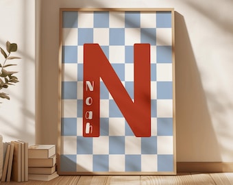 May include: A framed wall art print featuring a light blue and white checkered pattern background. A large, bold, solid red letter N is centered on the print, with the name Noah written vertically in white letters inside the red N.