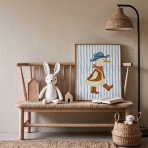 May include: A framed watercolor print of a duck wearing a cowboy hat, vest, and boots, set against a blue and white striped background. The print is displayed on a wooden bench with a stuffed bunny, wooden houses, and a woven basket.