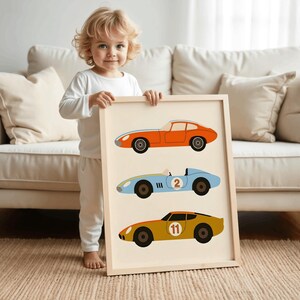 May include: A framed wall art print featuring three vintage-style race cars stacked vertically. The top car is orange, the middle light blue car displays the number 2, and the bottom mustard yellow car features the number 11 in a white circle.