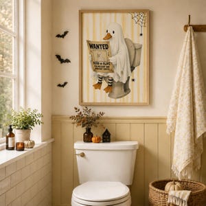 May include: A framed wall art print featuring a white ghost duck sitting on a toilet, holding a WANTED poster that reads DEAD OR ALIVE FOR MISCHIEF AND MIDNIGHT SNACKS. The background has yellow vertical stripes, a spider web, and small spiders.