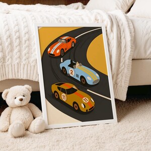 May include: A framed art print featuring a stylized illustration of three race cars driving on a curved track. The cars are orange, light blue with the number 2, and yellow with the number 11, all set against a yellow and dark gray background.