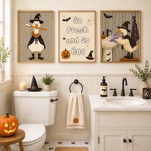 May include: Three framed wall art prints featuring a duck wearing a witch hat and cape, and text that reads So Fresh and So Boo. The prints display Halloween themes with pumpkins, bats, and ghosts against a striped background in a bathroom.