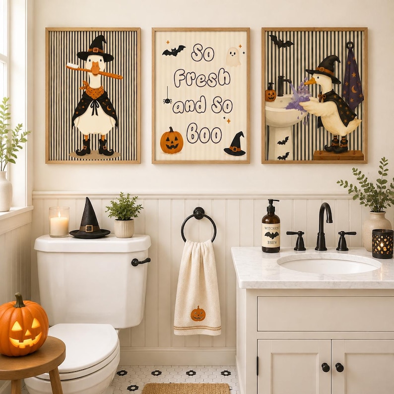 May include: Three framed wall art prints featuring a duck wearing a witch hat and cape, and text that reads So Fresh and So Boo. The prints display Halloween themes with pumpkins, bats, and ghosts against a striped background in a bathroom.