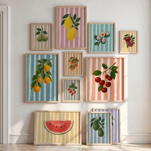 Könnte beinhalten: Eine Sammlung gerahmter Kunstdrucke mit farbenfrohen Obstillustrationen. Die Drucke zeigen verschiedene Früchte wie Zitronen, Kirschen und Wassermelonen vor gestreiften Hintergründen in Pastellfarben. Die Rahmen sind aus hellem Holz.