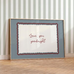 May include: A rectangular framed print featuring a white center with the dark red text Love you goodnight. The text is surrounded by a wavy, scalloped border in dark red and muted blue tones, set against a solid, muted blue background.