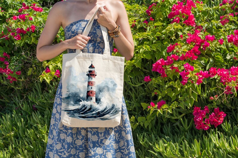 May include: A white canvas tote bag featuring a watercolour painting of a red and white lighthouse in the sea. The bag has a blue and white floral design.