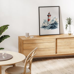 May include: A watercolour painting of a red and white lighthouse in a stormy sea. The painting is framed in black and hanging on a white wall above a wooden dresser.