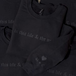 May include: Black crewneck sweatshirts with the phrase "in this life & the next" printed in a gothic font. One sweatshirt sleeve has a heart graphic and the initials "B+C".