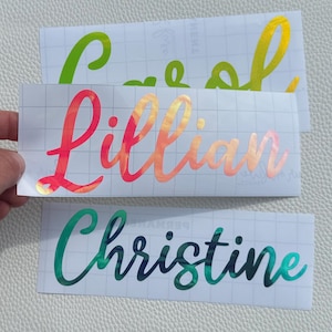 May include: Three rectangular adhesive vinyl decals featuring custom names in a cursive script font. The top decal is lime green, the middle decal is a gradient of pink to orange, and the bottom decal is a gradient of teal to dark blue.