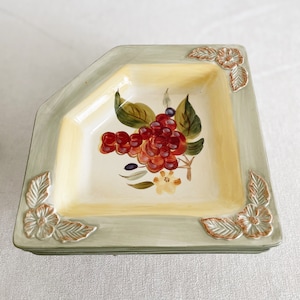May include: A green and yellow ceramic serving dish with a raised floral design around the edge. The dish features a painted design of red and purple grapes with green leaves.