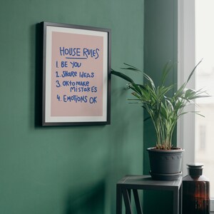 Pu&ograve; includere: Una stampa incorniciata con le parole "HOUSE RULES" in blu. Le regole sono elencate di seguito: "BE YOU", "SHARE IDEAS", "OK to make MISTAKES" e "EMOTIONS OK". La stampa &egrave; su sfondo rosa e incorniciata in nero.