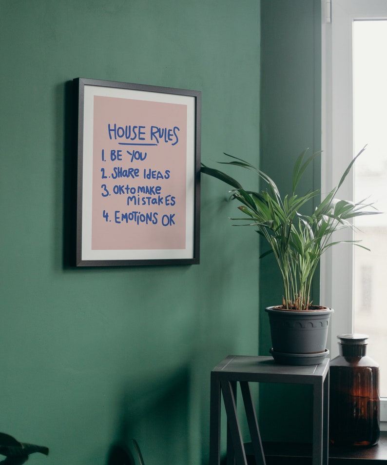 Pu&ograve; includere: Una stampa incorniciata con le parole "HOUSE RULES" in blu. Le regole sono elencate di seguito: "BE YOU", "SHARE IDEAS", "OK to make MISTAKES" e "EMOTIONS OK". La stampa &egrave; su sfondo rosa e incorniciata in nero.