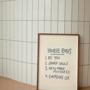 Pu&ograve; includere: Una stampa incorniciata con le parole "HOUSE RULES" e quattro affermazioni: "BE YOU", "SHARE IDEAS", "OK to MAKE MISTAKES" e "EMOTIONS OK". La stampa ha una cornice marrone ed &egrave; posta contro un muro di piastrelle bianche.