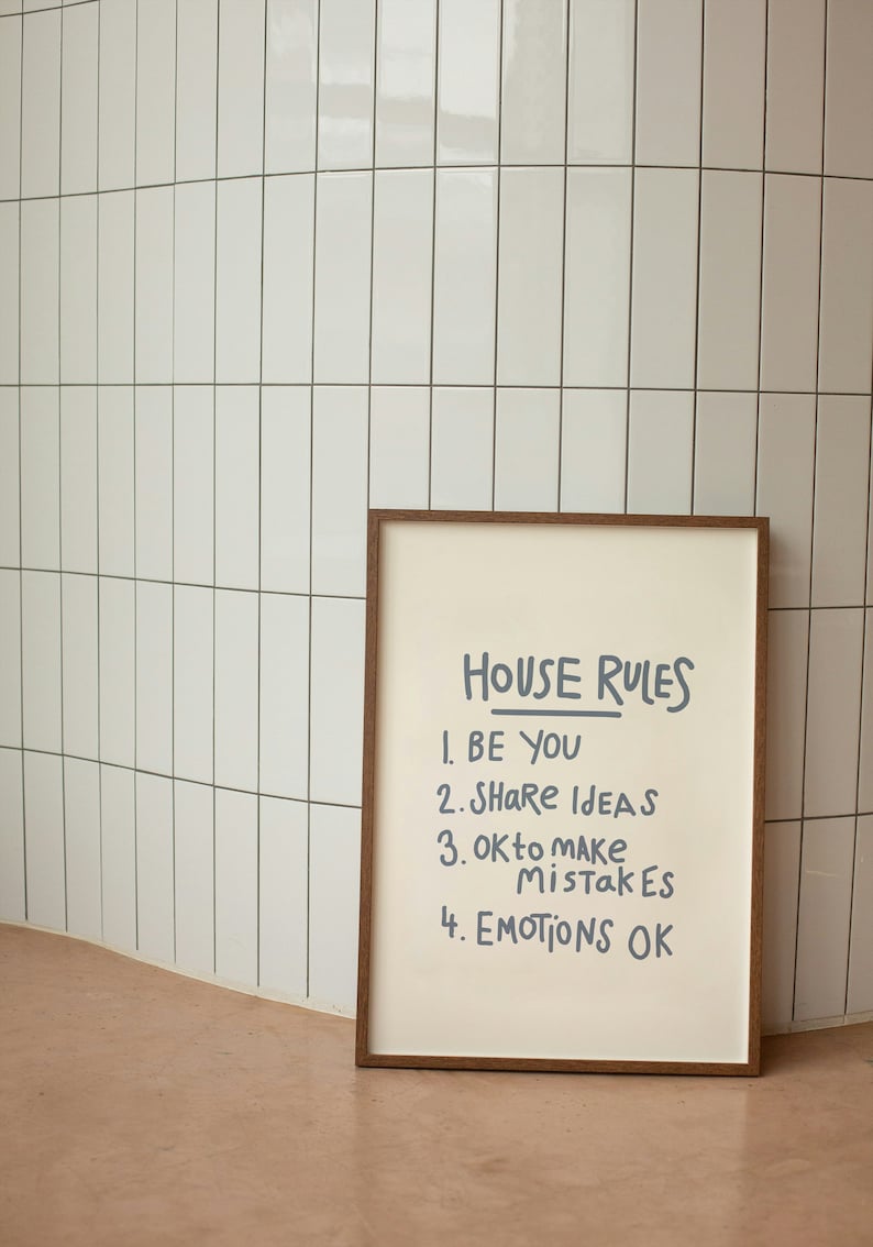 Pu&ograve; includere: Una stampa incorniciata con le parole "HOUSE RULES" e quattro affermazioni: "BE YOU", "SHARE IDEAS", "OK to MAKE MISTAKES" e "EMOTIONS OK". La stampa ha una cornice marrone ed &egrave; posta contro un muro di piastrelle bianche.