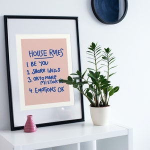 Pu&ograve; includere: Una stampa incorniciata con le parole "HOUSE RULES" e un elenco di quattro regole in inchiostro blu su sfondo rosa. Un piccolo vaso rosa e una pianta in vaso sono su una mensola bianca.