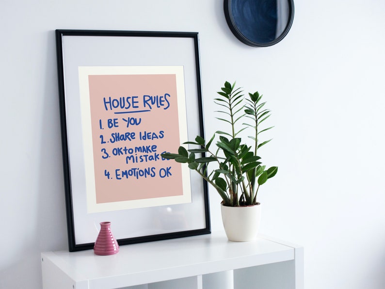Pu&ograve; includere: Una stampa incorniciata con le parole "HOUSE RULES" e un elenco di quattro regole in inchiostro blu su sfondo rosa. Un piccolo vaso rosa e una pianta in vaso sono su una mensola bianca.
