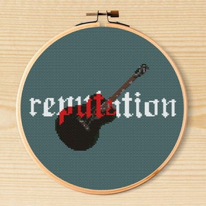 May include: Cross-stitch embroidery hoop with a blue background, a black and red acoustic guitar, and the word "reputation" in white text.