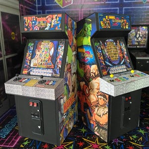 May include: Two arcade game machines with colorful Marvel vs. Capcom graphics. The machines have joysticks, buttons, and screens displaying game characters. The cabinets are black with detailed artwork.