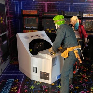 May include: A white arcade cabinet with a black and green figure standing next to it. The cabinet has a black screen and a white control panel. The figure is wearing a green mask and a blue jumpsuit. The background is a brick wall with neon lights.