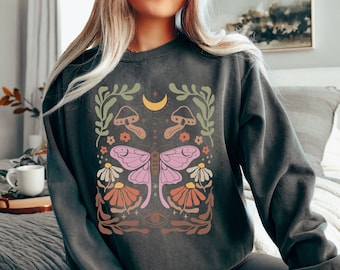 May include: A dark gray sweatshirt with a graphic print of a pink butterfly, mushrooms, flowers, and a crescent moon. The design is in a vintage style with a faded look.
